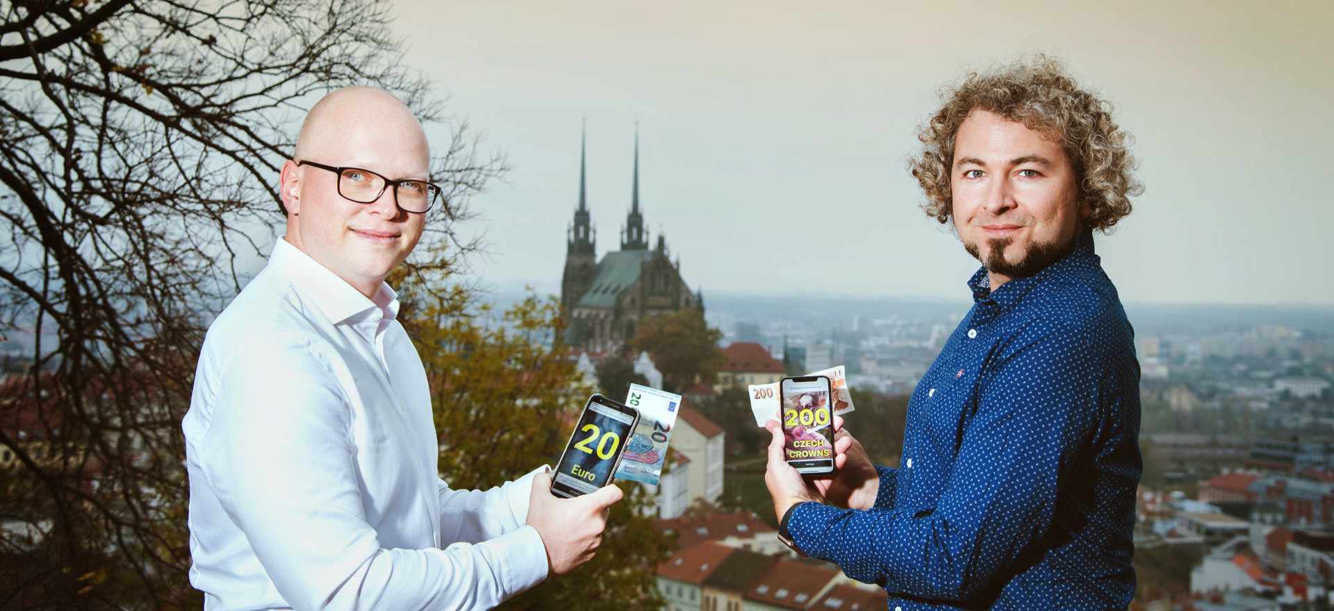Cash Reader founders Tomas and Martin holding smartphones displaying the app, with the city of Brno and its cathedral in the background